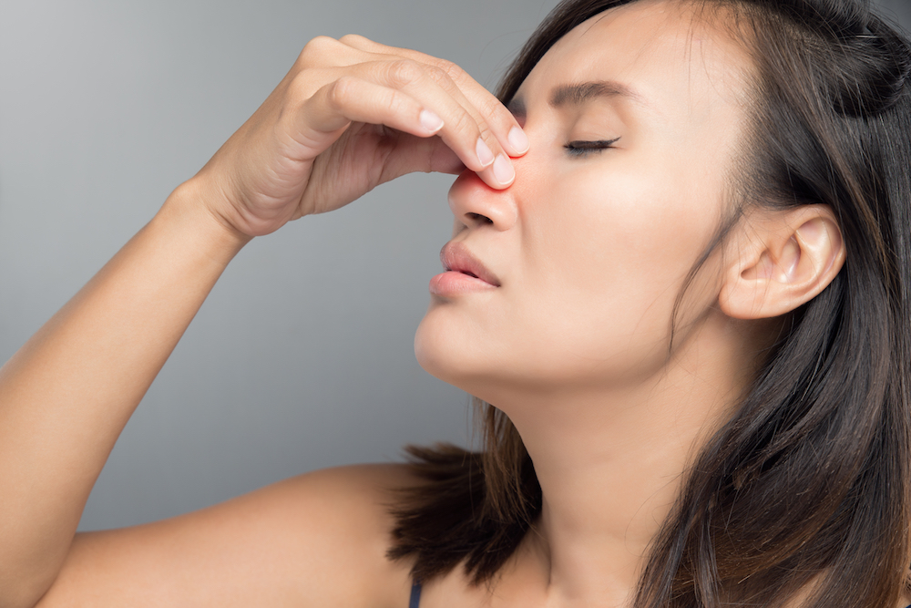 A woman holds the bridge of her nose and tilts her head back