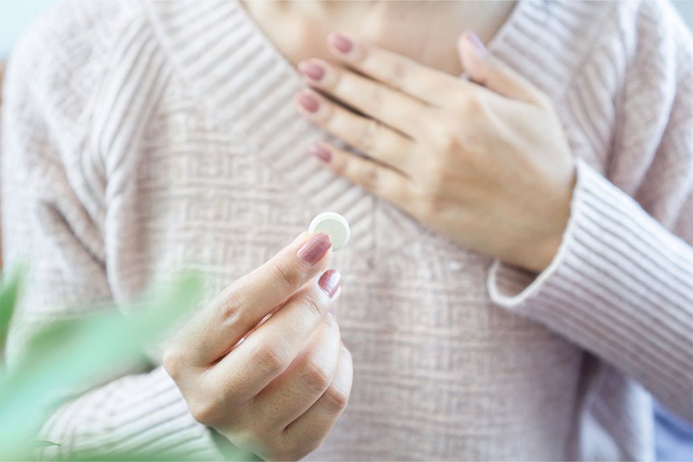 A woman clutches her chest and holds an antacid in one hand.